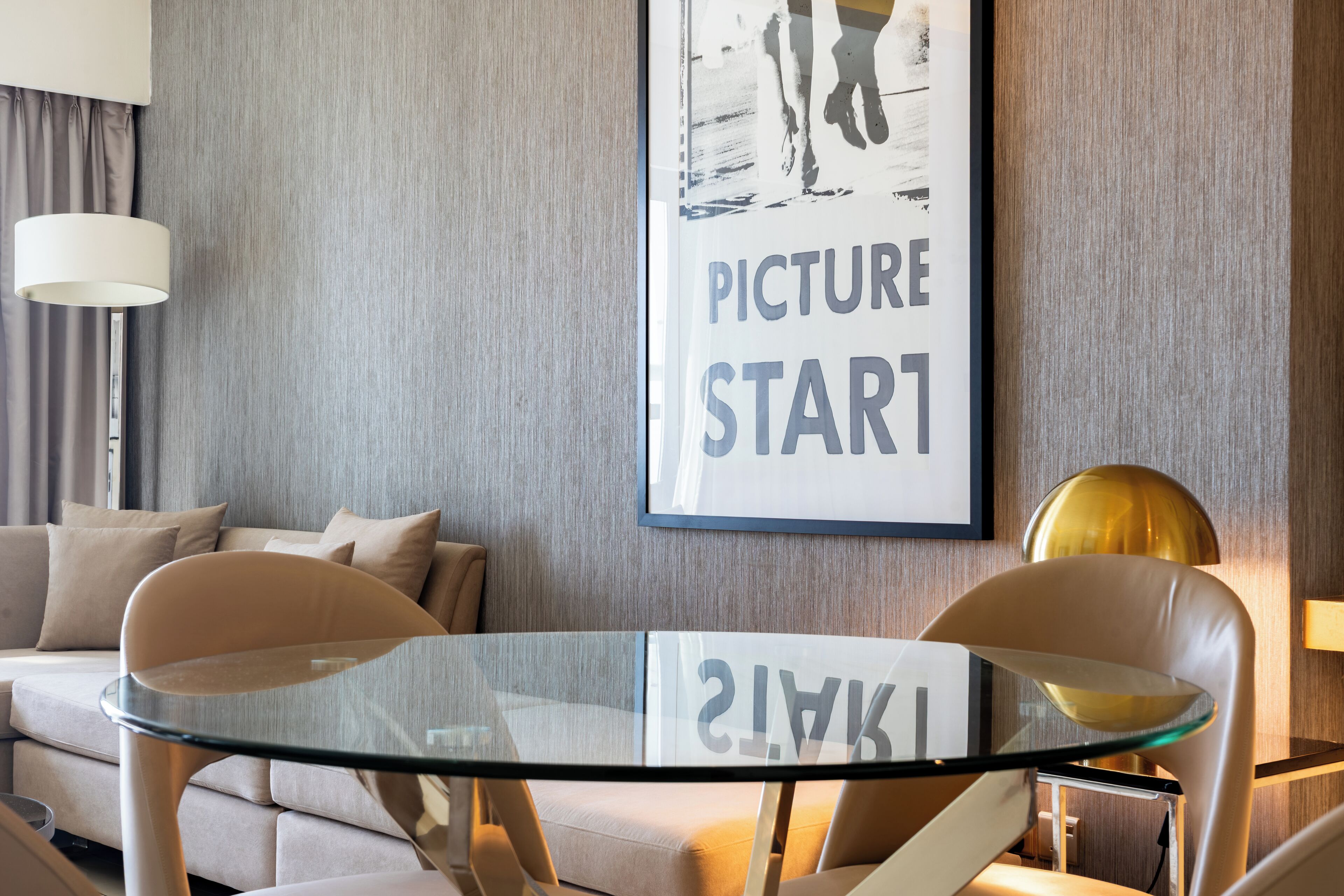 Un salon moderne avec une table à plateau en verre, deux chaises, un canapé et un tableau encadré accroché au mur.