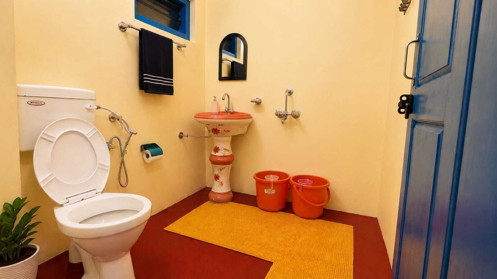 A bathroom with a toilet, sink, and two buckets on the floor.
