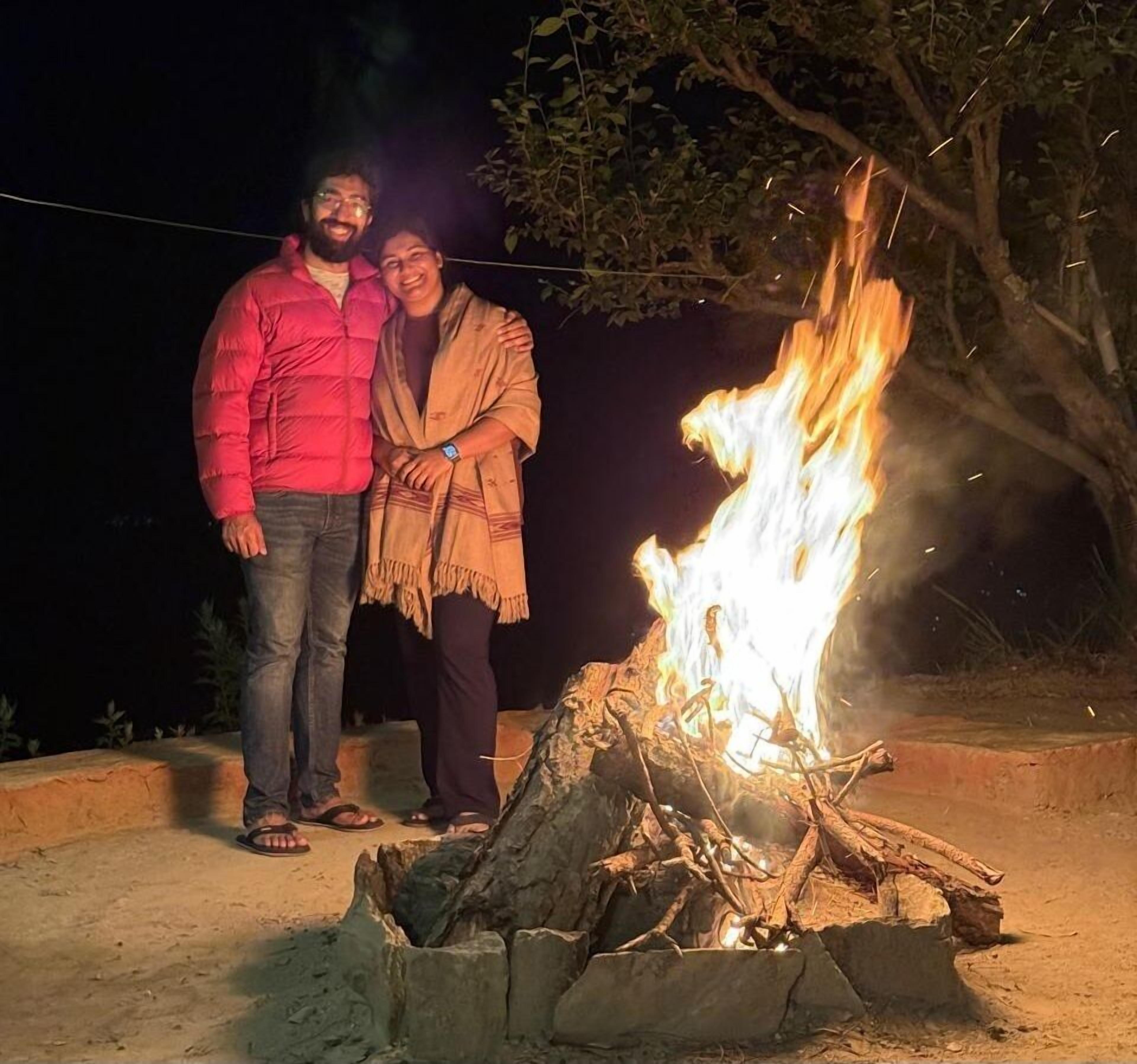 Two people standing by a campfire at night.