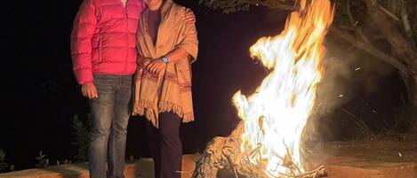 Two people standing by a campfire at night.