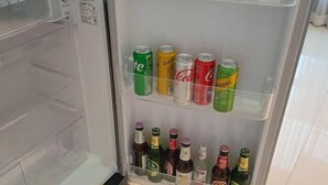 Egy nyitott hűtőszekrény, melynek polcain különféle italok találhatók, köztük dobozos és üveges italok.