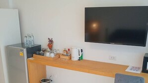 Egy kis konyhasarok, amelyben van egy hűtőszekrény, egy fa pult, a falra szerelt televízió és egy szürke szék.