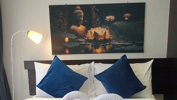Egy szállodai szoba, amelyben egy ágy, két kék párna, egy Buddha-kép és két törölköző található, melyeket szív alakban helyeztek el.