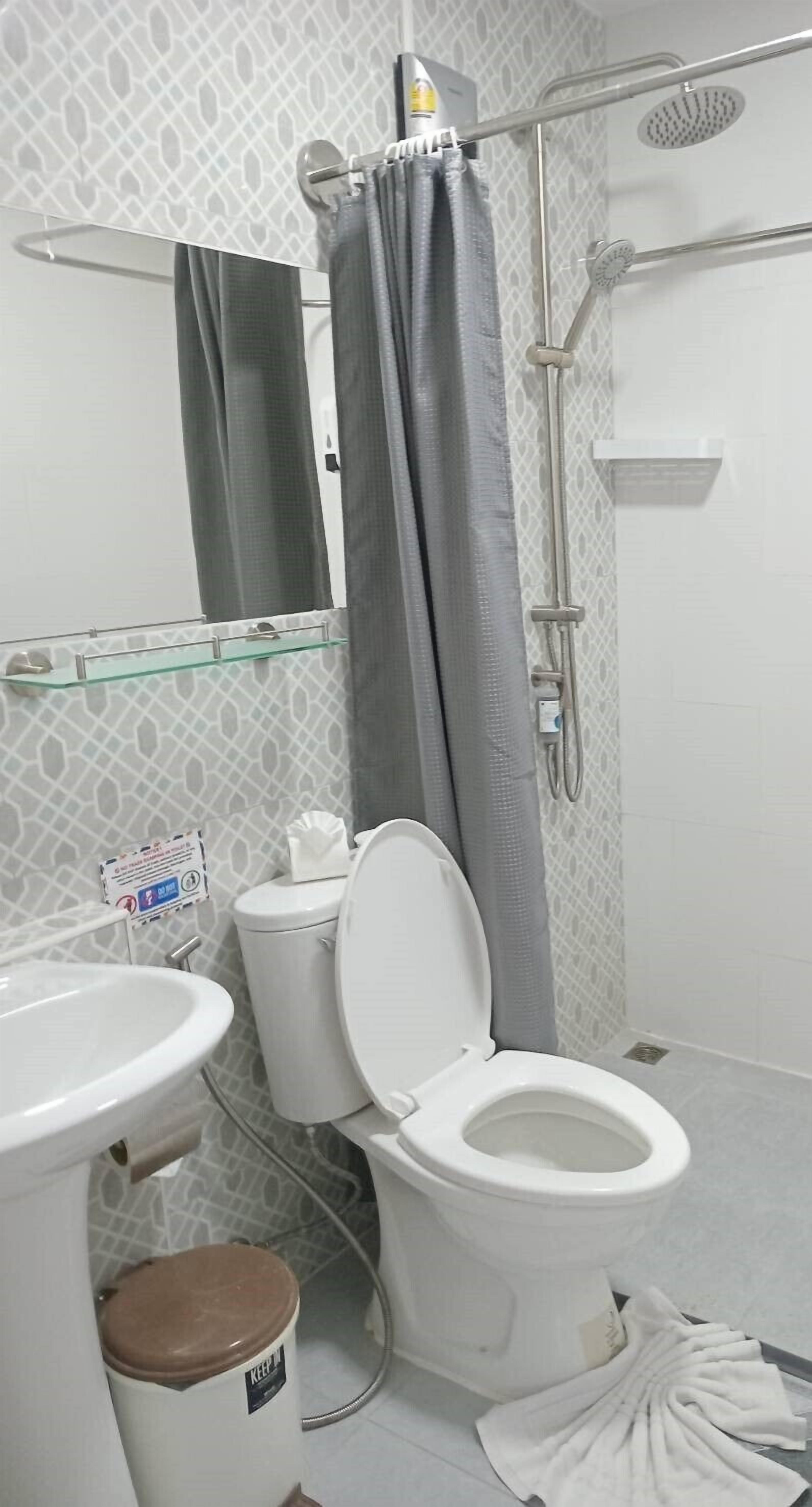 Un baño con inodoro, lavamanos, ducha y estante de vidrio.