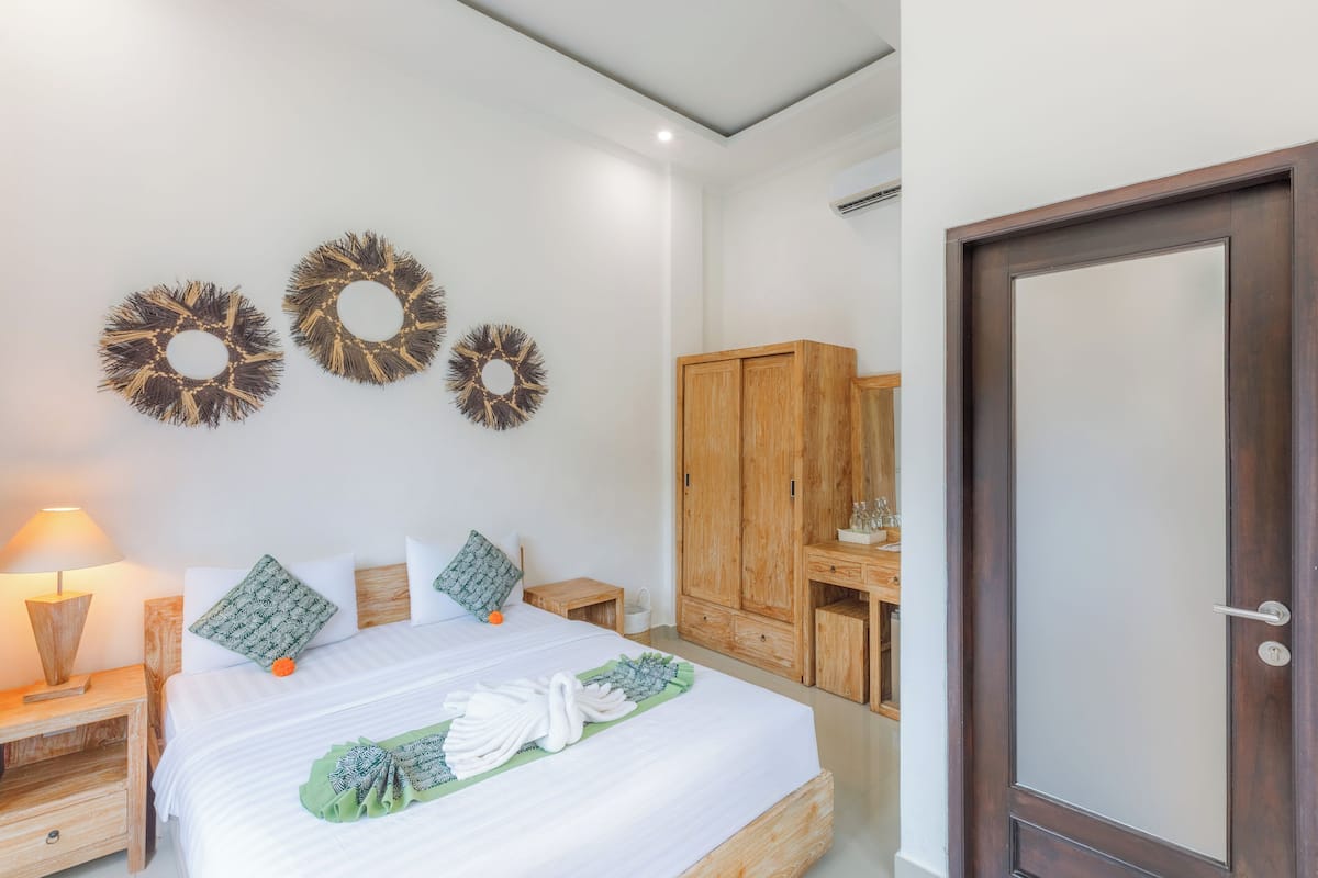Una cama bien hecha con una toalla verde y una colcha blanca, mesitas de noche de madera, un armario de madera y adornos en la pared.