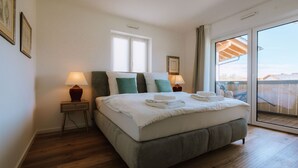 Ein Schlafzimmer mit einem großen Bett, zwei Nachttischen mit Lampen, einem Fenster und einem Balkon mit Aussicht.