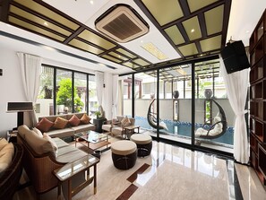 A spacious living area with a sofa set, a glass coffee table, and a view of a swimming pool. - Lumiere Villa Nam Thong Phu My Hung (Ho Chi Minh City)