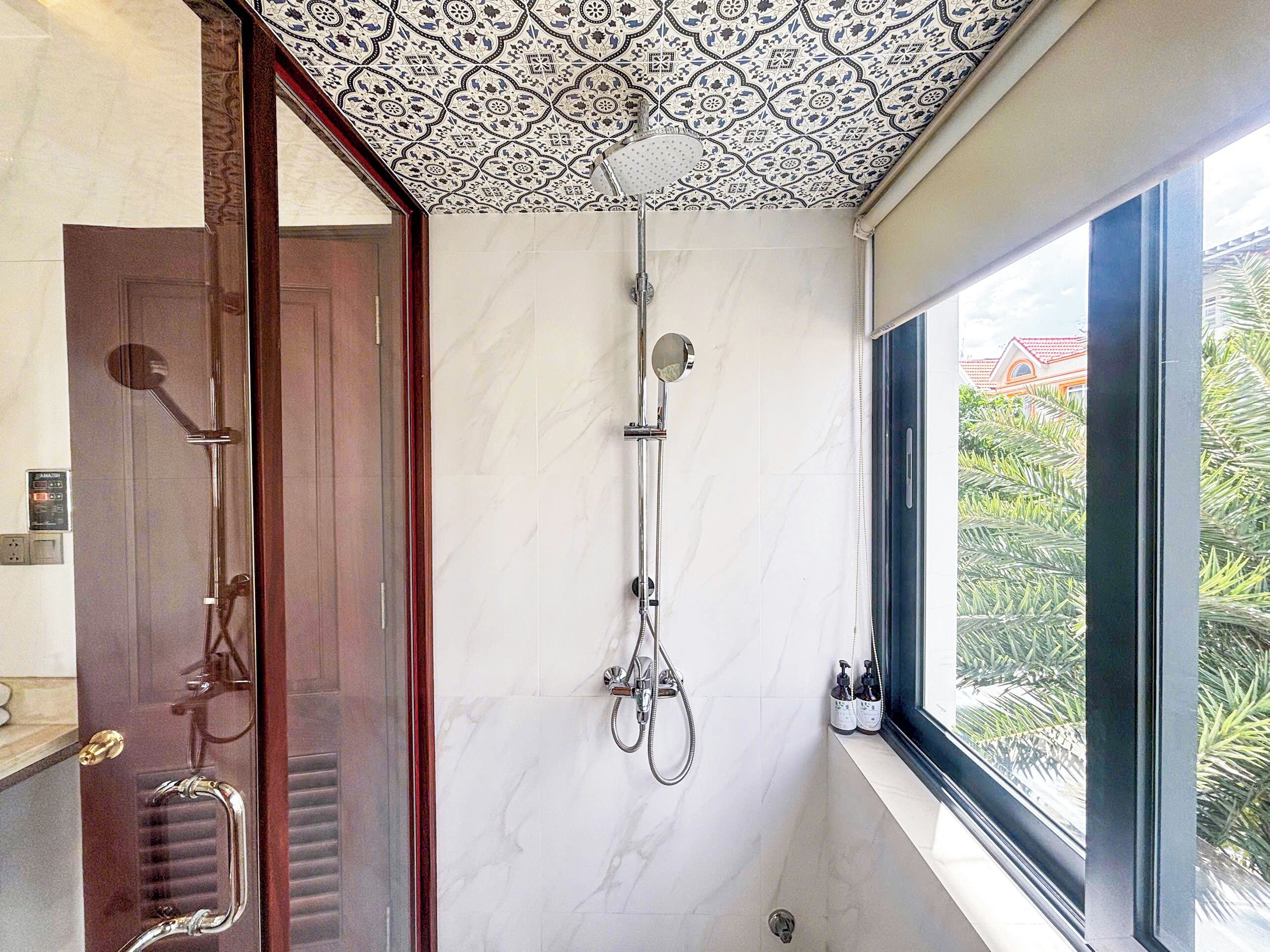 Un baño con ducha, una ventana que da a zonas verdes y un techo con diseño.