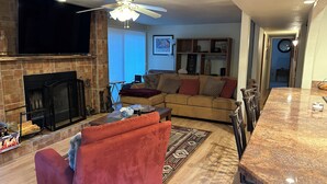 A living room with a fireplace, a sofa, a red armchair, a dining area with a marble table, and a ceiling fan. - 2-bedroom home in Sedona on the creek (Sedona)