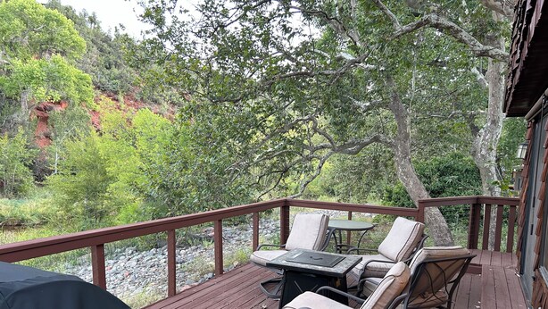 A wooden deck with outdoor furniture, a grill, and a view of a forested area. - 2-bedroom home in Sedona on the creek (Sedona)