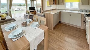 A compact kitchen with a dining area, a TV, and a view of a fenced yard. - Birch 2 Bedroom Pet Friendly (Clynderwen)