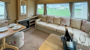 A cozy RV interior with a sofa, a dining table, and a TV. - Birch 2 Bedroom Pet Friendly (Clynderwen)