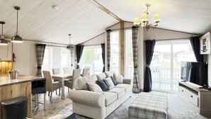 A spacious living area with a sofa, ottoman, dining table, and chairs, a kitchen area with a TV, and large windows with curtains. - 1 bedroom accommodation in Chester (Chester)