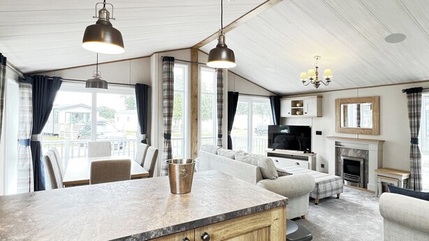 A modern kitchen with a central island, a dining area with a table and chairs, a living room with a sofa and a fireplace, and large windows with curtains. - 1 bedroom accommodation in Chester (Chester)