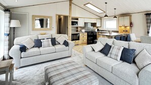A modern living room with two grey sofas, a plaid ottoman, and a kitchen in the background. - 1 bedroom accommodation in Chester (Chester)