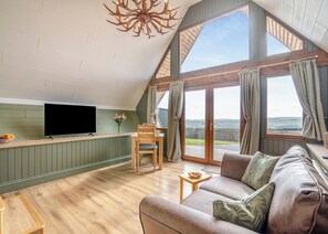 A spacious loft-style room with a large window, a television, a wooden dining table, and a comfortable seating area. - 1 bedroom accommodation in Ripponden (Ripponden)