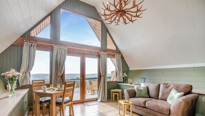 A cozy loft bedroom with a large skylight, wooden floor, a brown leather sofa, and a dining area with a table and chairs. - 1 bedroom accommodation in Ripponden (Ripponden)