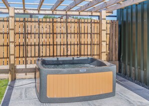 A hot tub in an outdoor setting with a wooden fence and a metal structure in the background. - 1 bedroom accommodation in Ripponden (Ripponden)