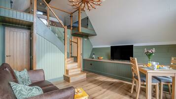 A spacious loft with a wooden staircase, a dining area with a TV, and a cozy seating area with a leather couch.