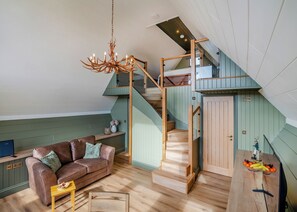 Un espace de vie de style loft comprenant un escalier, un canapé, une table en bois et un lustre.