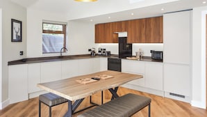 A modern kitchen with white cabinets, a wooden dining table, and a black pendant light.