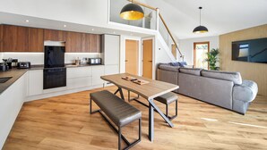 A modern kitchen with a dining area, a staircase, and a living room with a sofa.