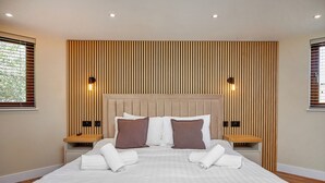A modern hotel room with a large bed, wooden slat headboard, bedside lamps, and a view of greenery through the window.