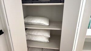 Un placard avec des étagères où sont rangés des vêtements pliés et des oreillers.