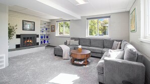 Een moderne woonkamer met een open haard, grijze banken, een salontafel en grote ramen.