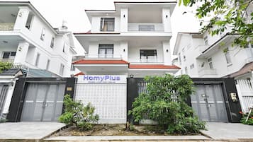 Un edificio residencial con entrada protegida por una reja, un letrero que dice 'HomyPlus' y una pequeña área ajardinada.