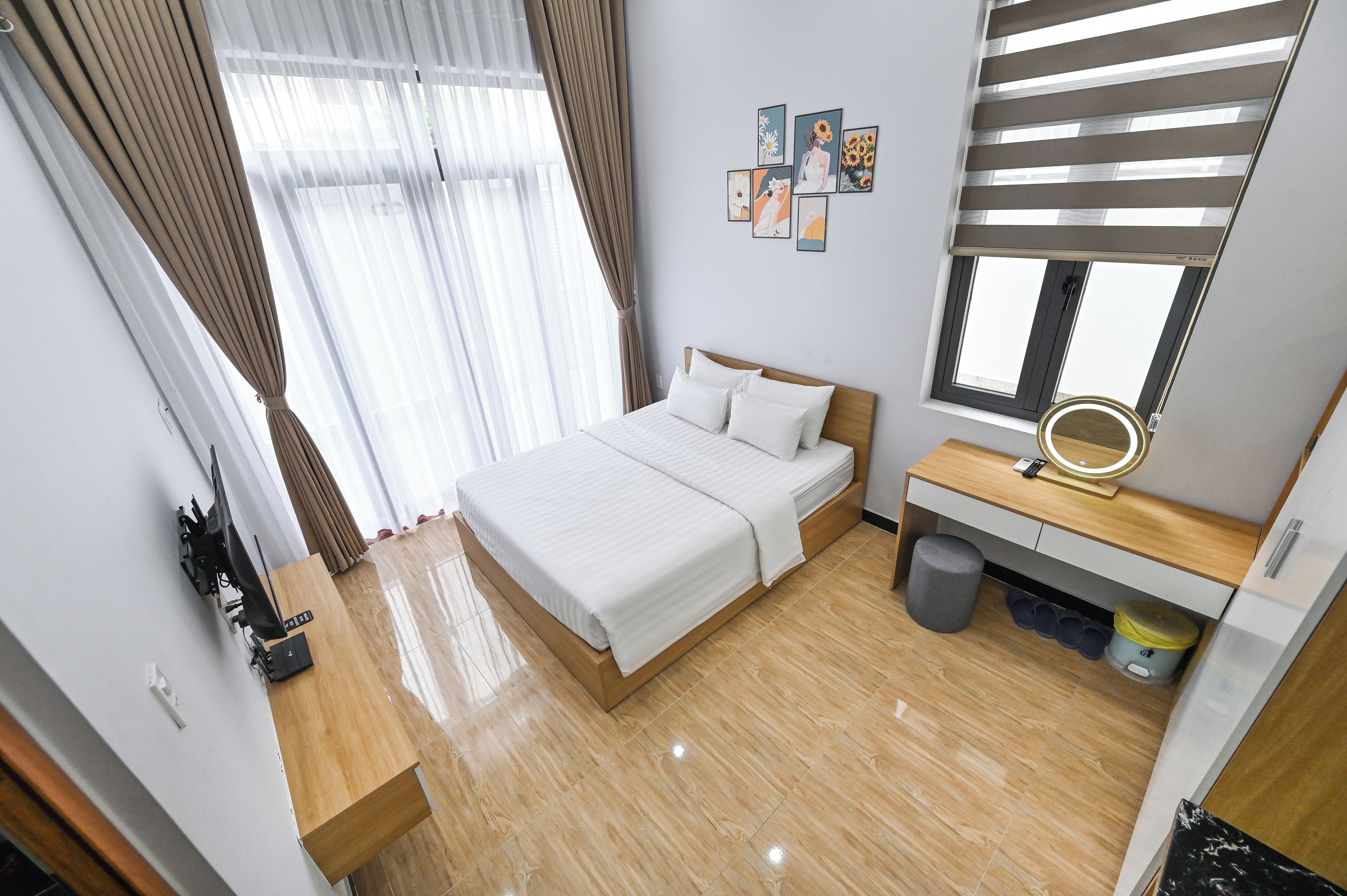 Ein Hotelzimmer mit einem Bett, einem Nachttisch mit Spiegel, einem kleinen Hocker, einem Mülleimer und einem an der Wand befestigten Fernseher.