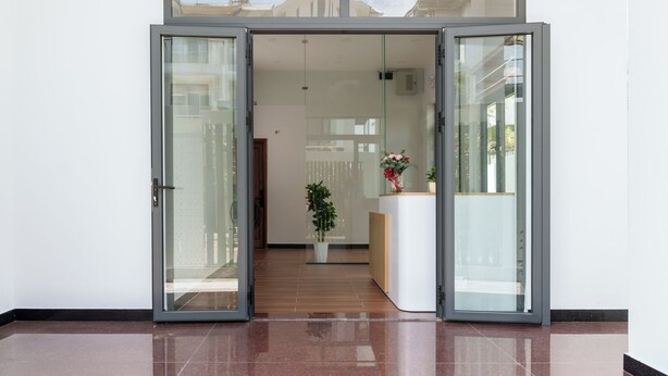 Een modern interieur met een glazen toegangsdeur, een receptiebalie en een potplant.