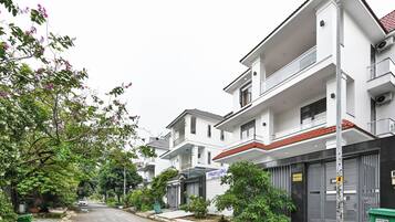 A residential street with modern two-story houses, a visible storefront, and a green trash bin.