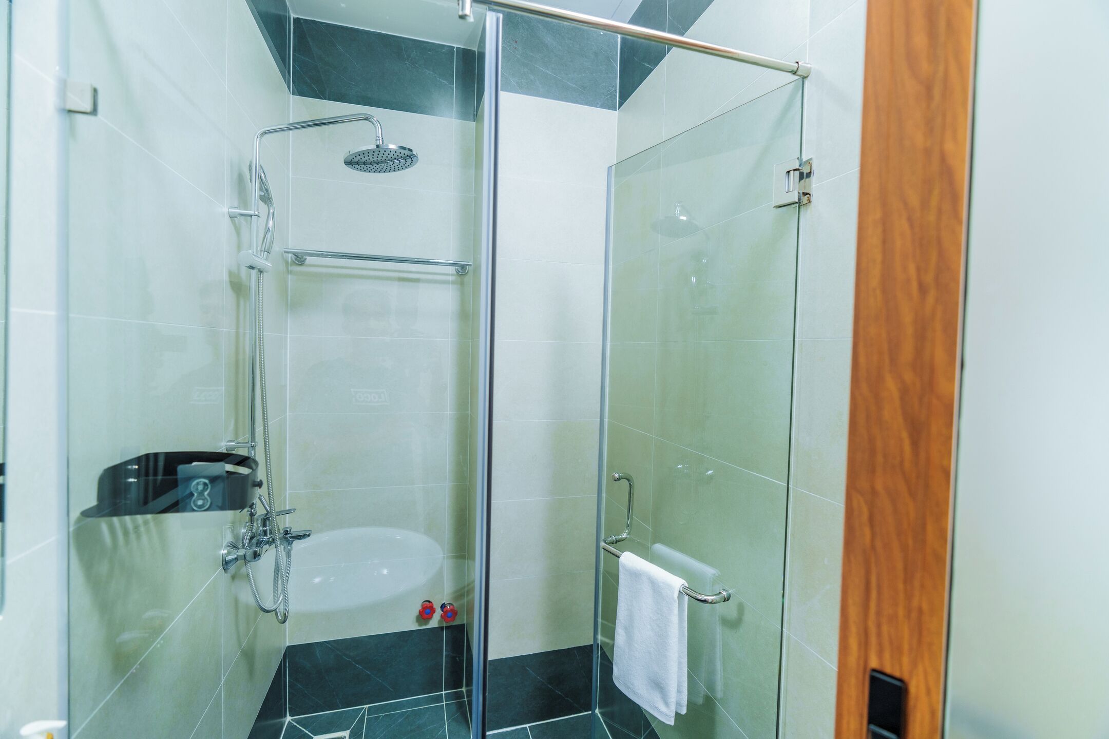 A glass-enclosed shower with a handheld showerhead and a handheld faucet.