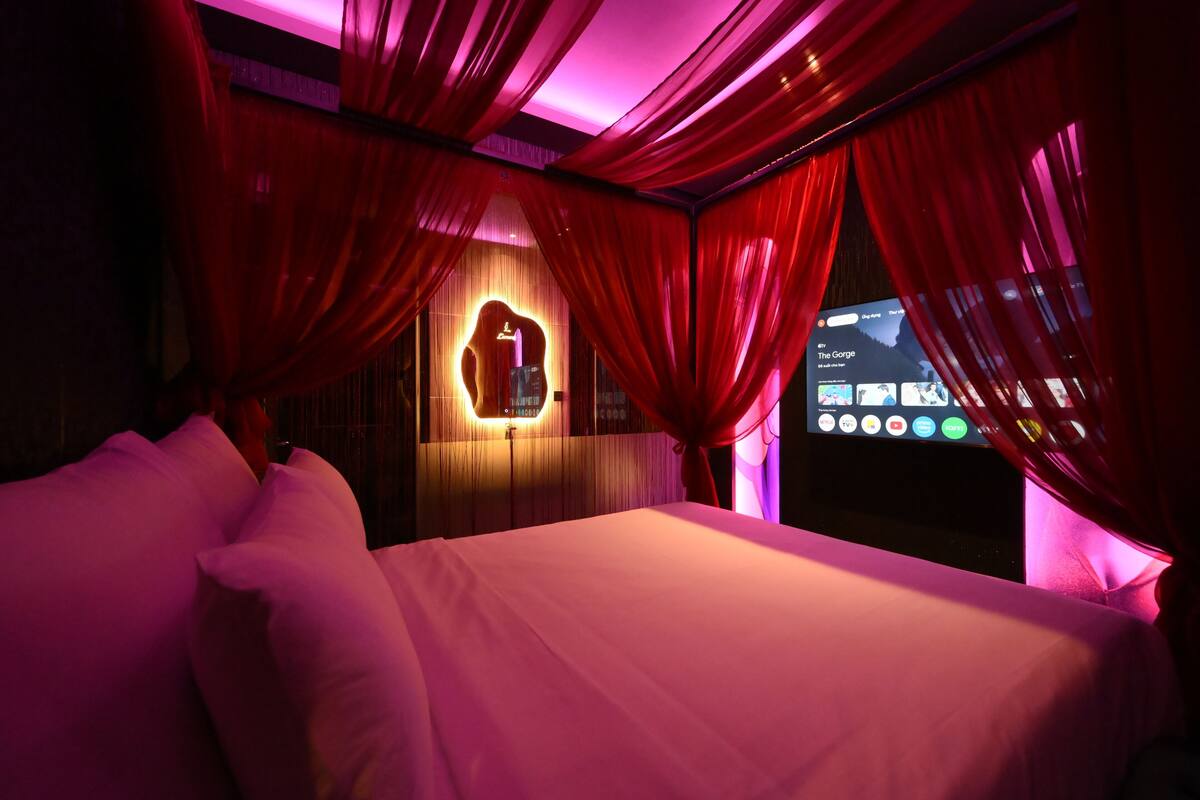 A hotel room with a bed, red curtains, and a wall-mounted TV displaying a music app.