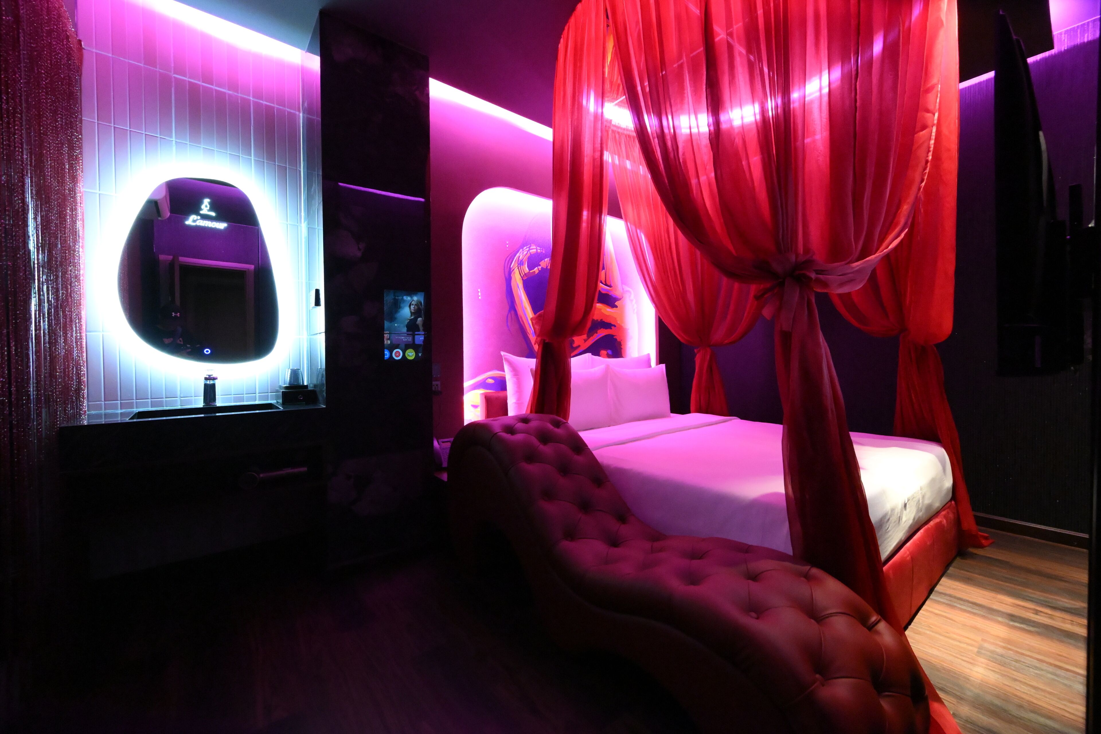 Un dormitorio con cama con dosel, tocador con espejo y televisor montado en la pared.
