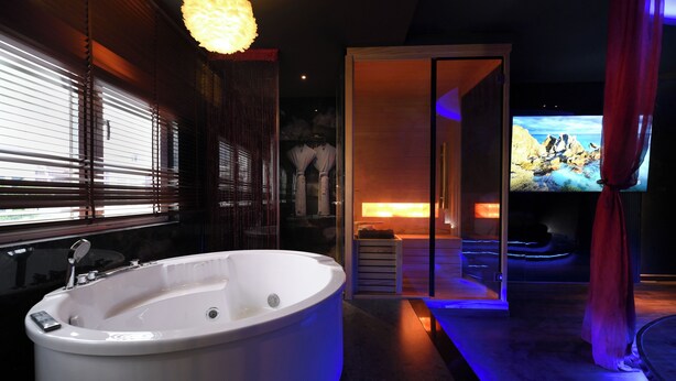 Une salle de bain moderne dotée d’une grande baignoire, d’un espace douche et d’un écran de télévision diffusant un paysage pittoresque.