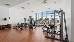 Ein geräumiger Fitnessraum mit unterschiedlichen Trainingsgeräten, großen Fenstern und Holzboden.