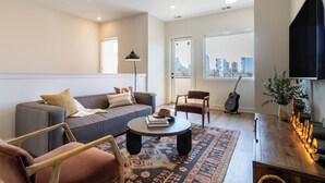 Una sala de estar moderna con sofá, sillones, una mesita de centro y vistas a la ciudad a través de amplios ventanales.