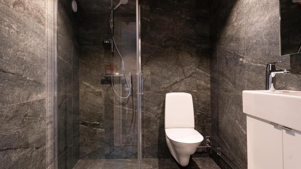 Un baño moderno con ducha envuelta en vidrio, inodoro blanco y lavabo blanco con espejo sobre él.