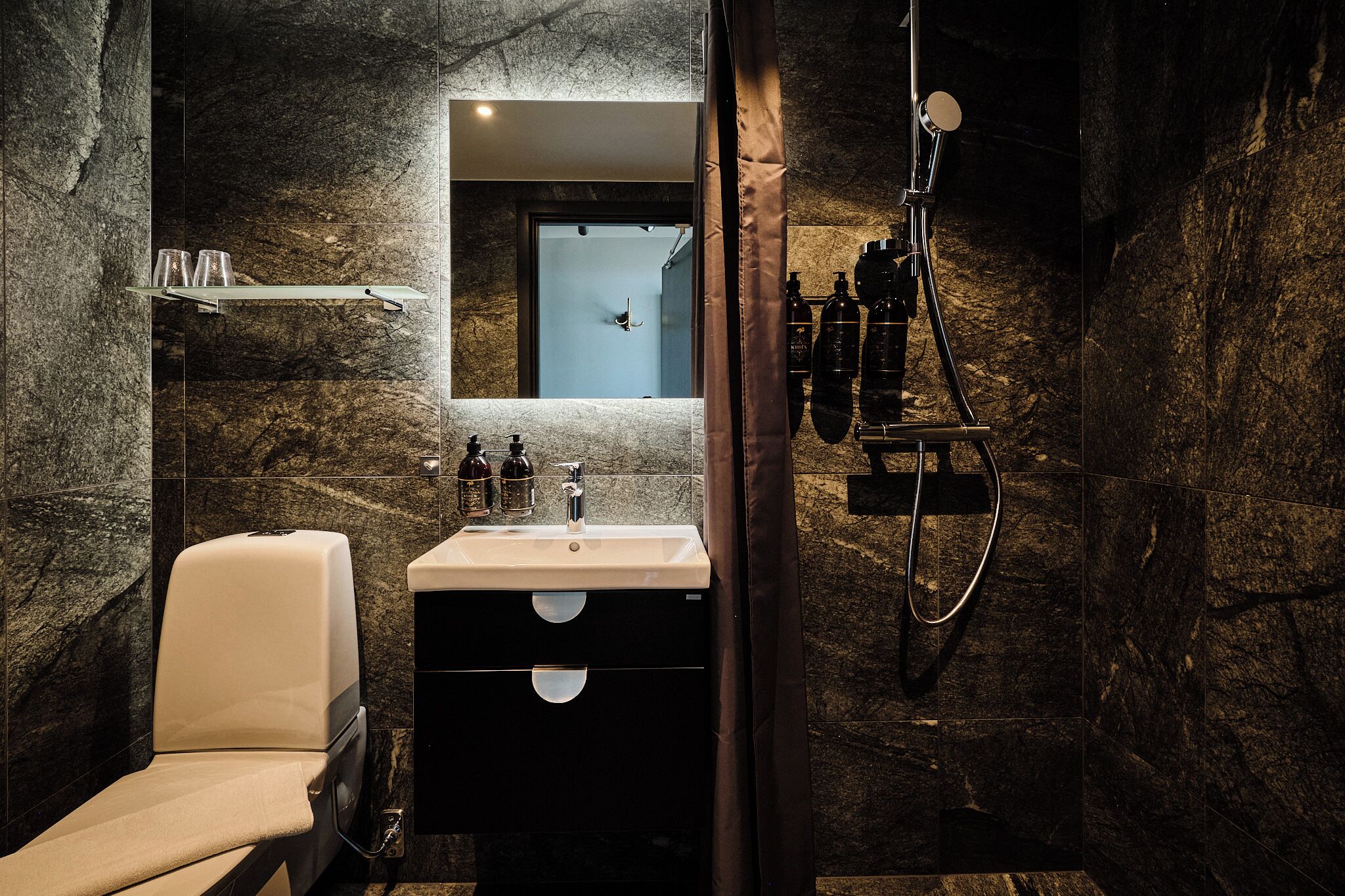 Un baño moderno con pared de mármol, un lavamanos blanco, un espejo y una ducha.