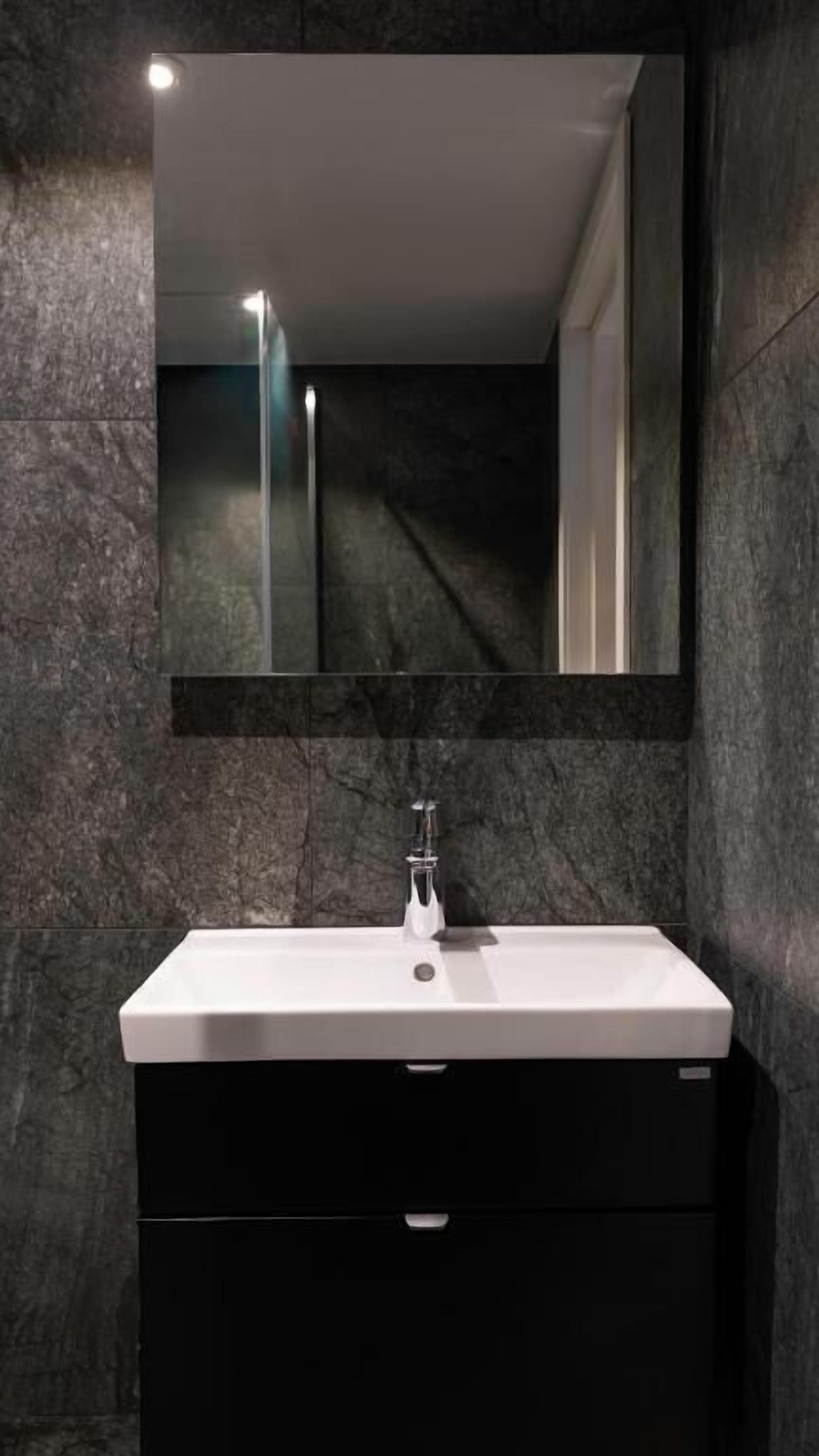 A modern bathroom with a white sink, dark marble walls, and a large mirror above the sink.