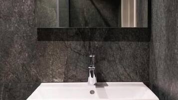 A modern bathroom with a white sink, dark marble walls, and a large mirror above the sink.