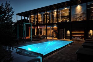Una casa moderna con piscina, mobiliario de exterior y un patio cubierto.