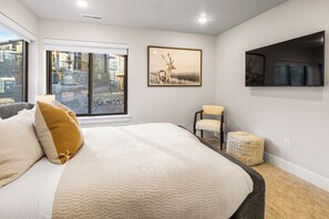 Une chambre avec un grand lit, une fenêtre donnant sur un chantier de construction, un tableau représentant un cerf encadré, une télévision et un petit pouf.