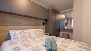 A hotel room with a bed featuring a patterned bedspread, a wooden headboard, and two rolled towels on the bed. - Paddington's Place – A Luxurious Seaside Escape in Mudeford (Christchurch)