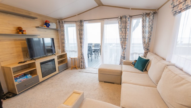 A modern living room with a sofa, TV, wooden shelves, and a balcony with outdoor furniture. - Paddington's Place – A Luxurious Seaside Escape in Mudeford (Christchurch)