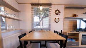 A dining area with a wooden table, black chairs, and a window with blinds. - Paddington's Place – A Luxurious Seaside Escape in Mudeford (Christchurch)