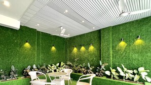 A room with green artificial grass walls, white wicker furniture, and a checkered floor. - Hill Top Heaven By Elvora Hotels & Resorts (Kasauli)