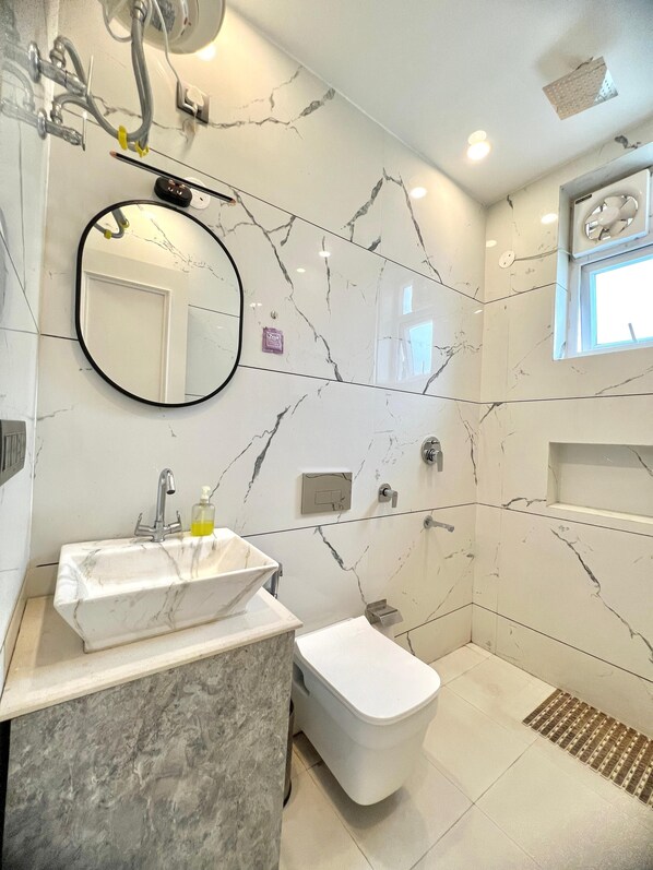 Un baño con lavamanos de mármol, inodoro y zona de ducha.